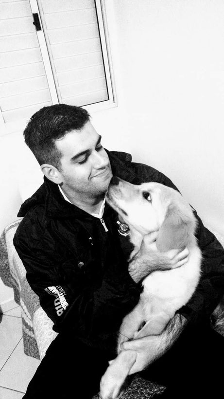 Foto em preto e branco: Anderson sentado abraça um filhote de golden que lambe o seu queixo.